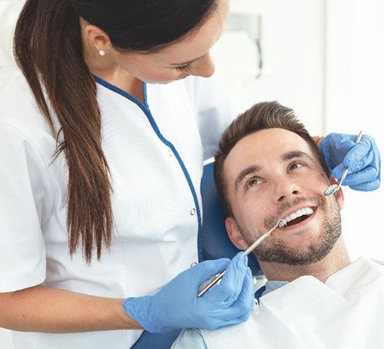 A dental hygienist prepares to start a dental cleaning while the male patient smiles