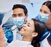 Patient smiling at reflection with dentist and dental assistant