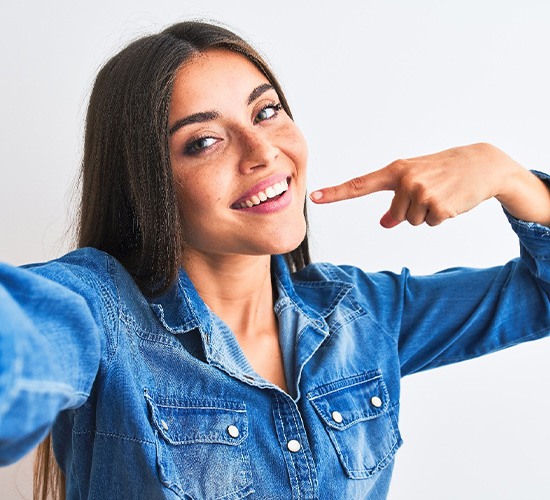 Woman smiling while pointing to her white teeth