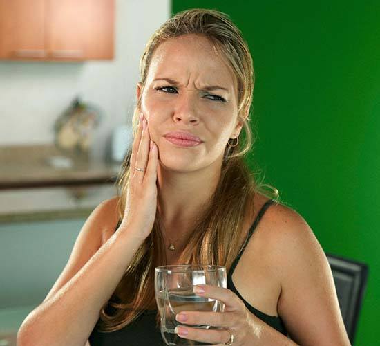 Woman with a toothache in Rockledge holding glass of water