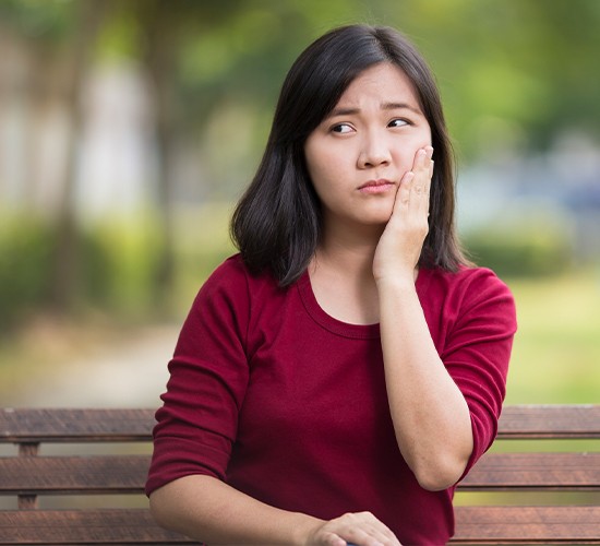 woman in red shirt on bench holding cheek