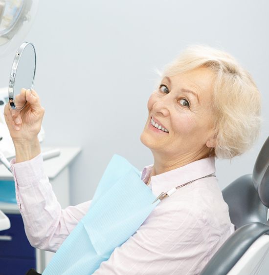An older woman smiling and holding up a handheld mirror after receiving her affordable implants in Rockledge