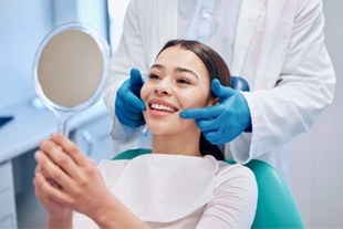 Woman smiling while looking at reflection in dentist's mirror