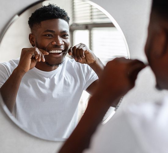 Man smiling while flossing his teeth in bathroom