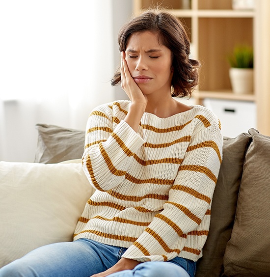 woman sitting on couch holding cheek in pain
