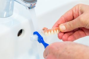 Someone holding their dentures under running water to brush them