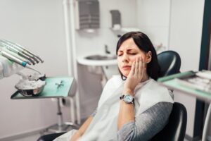 Young woman sitting in dentist's chair clutching her jaw in pain.